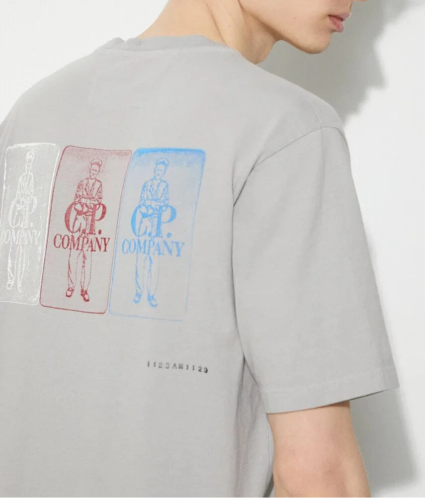 Person wearing a gray t-shirt with brand logos CP Company on the back against a white background