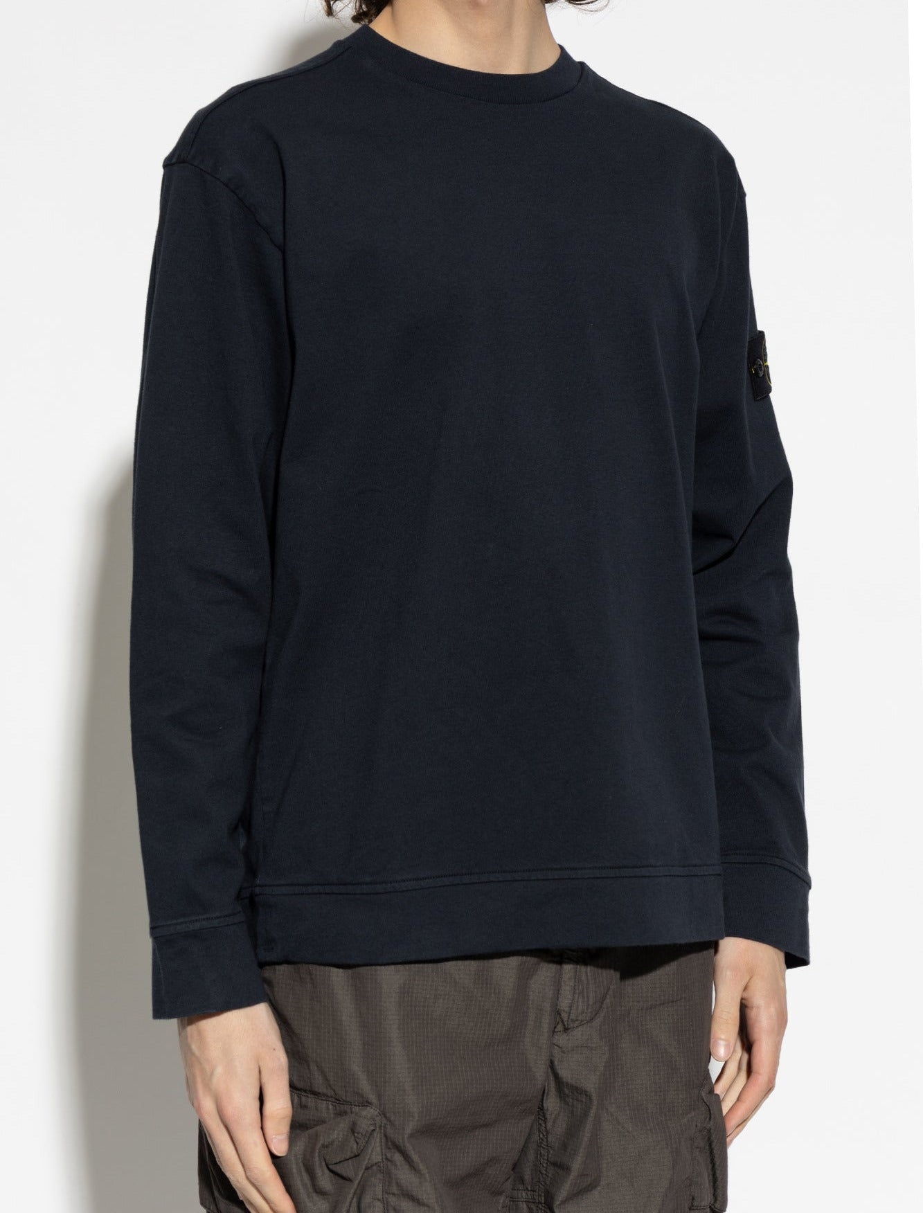 Person wearing a navy Stone Island sweatshirt and dark pants against a white background