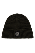 A black ribbed knit beanie hat featuring a small black square patch on the front cuff with the circular Stone Island compass logo. 