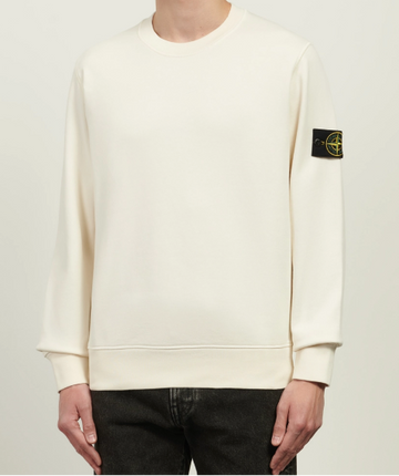 Person wearing a cream-colored Stone Island sweatshirt with a logo on the chest against a plain background