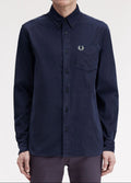 A man wearing a dark navy long-sleeve button-up shirt by Fred Perry, featuring the signature embroidered laurel wreath logo on the left chest pocket, set against a plain light gray background.