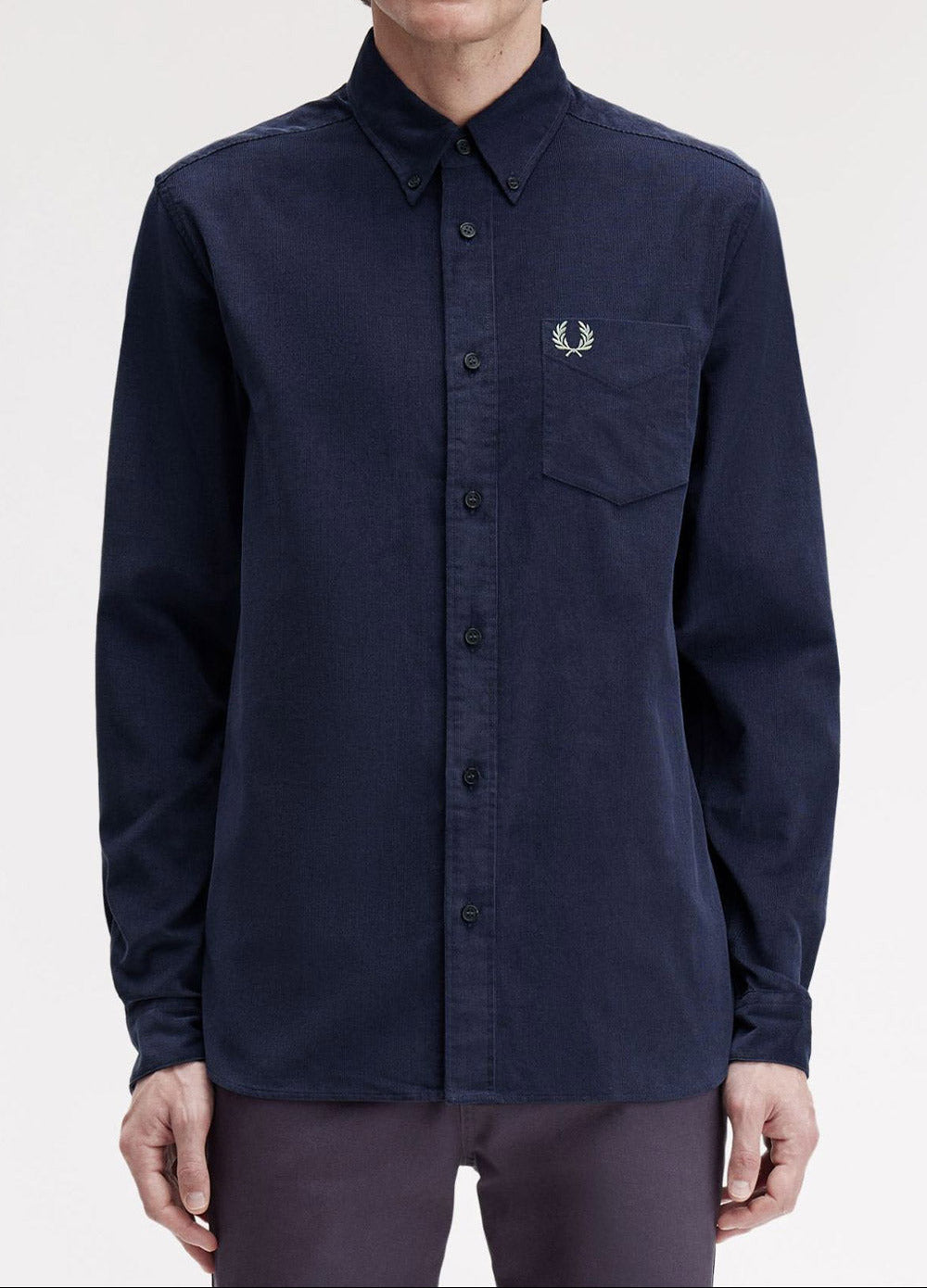 A man wearing a dark navy long-sleeve button-up shirt by Fred Perry, featuring the signature embroidered laurel wreath logo on the left chest pocket, set against a plain light gray background.