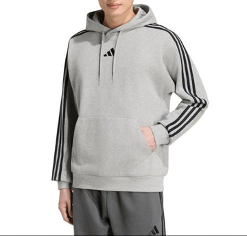 A man wearing a light gray Adidas hoodie with black three-stripes on the sleeves and a black logo on the chest, paired with gray track pants, against a plain white background.