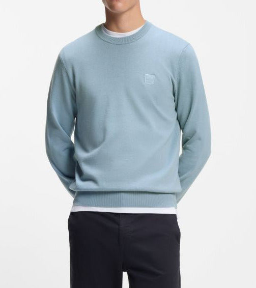 Man wearing a light blue sweater and dark pants on a white background