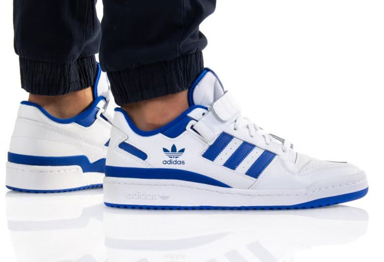 White Adidas sneakers with blue stripes worn by a person on a white background