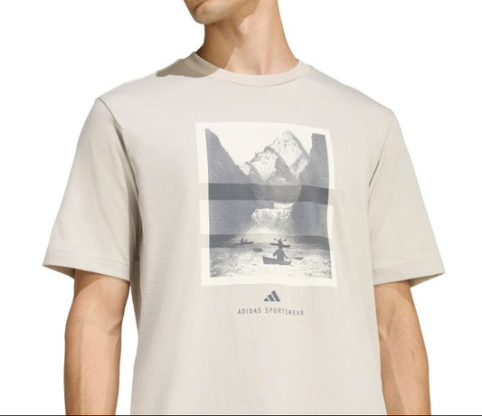 Man wearing a beige t-shirt with a graphic design and Adidas logo.